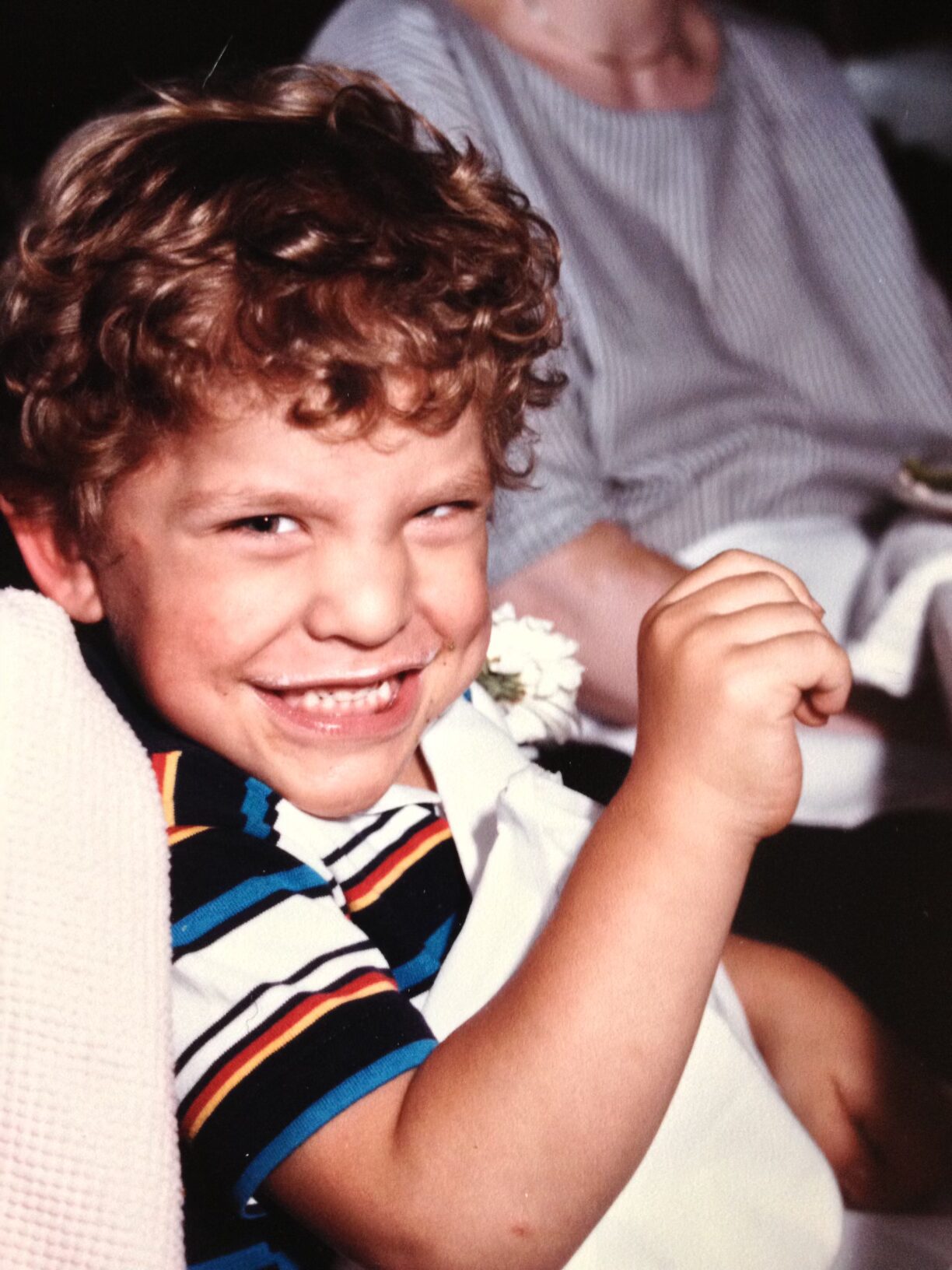 A young boy with curly hair smiles at the camera
